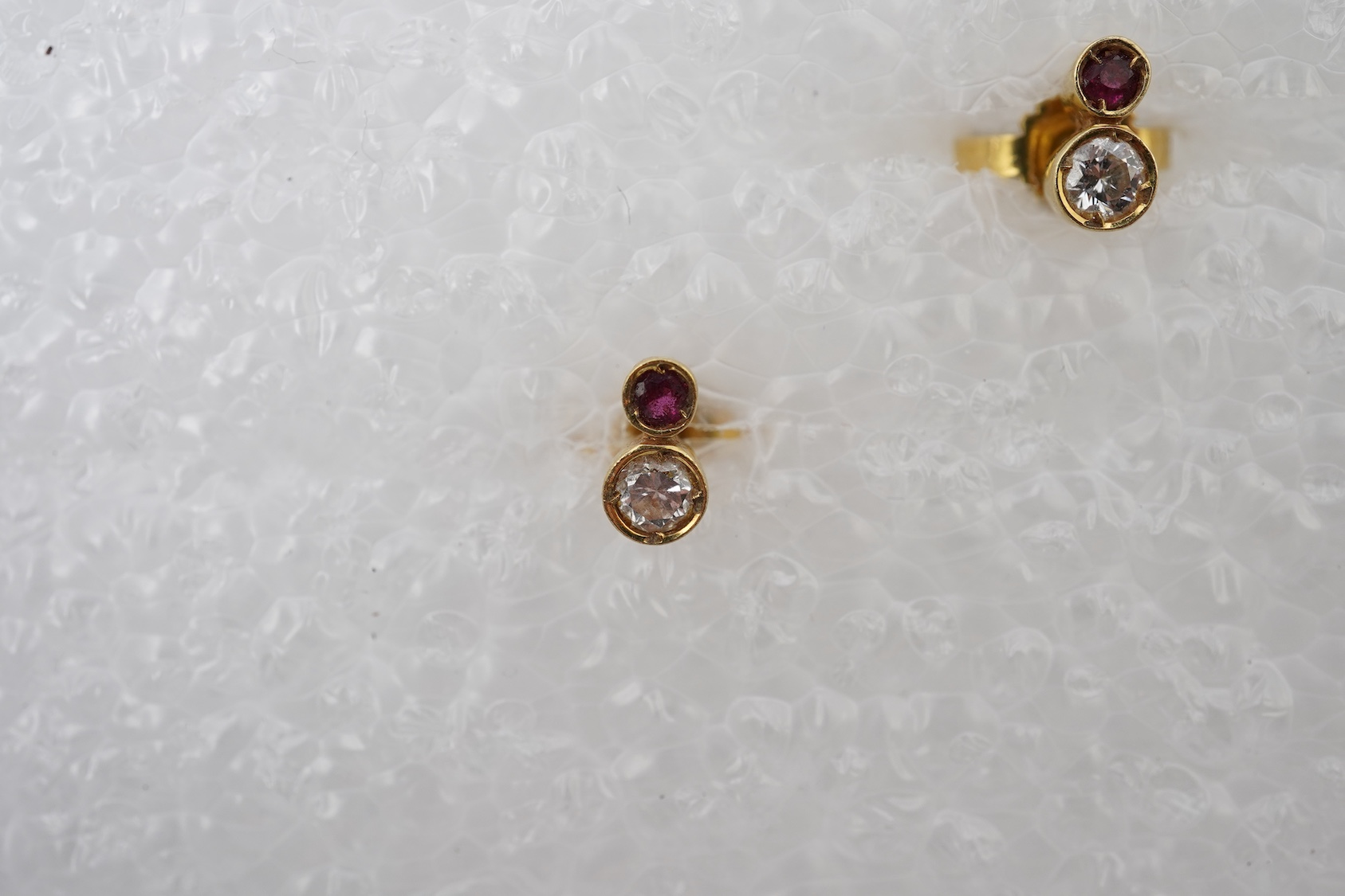 A pair of ruby and diamond stud earrings, set with brilliant-cut diamonds totalling approximately 0.15 carats, surmounted by circular-cut rubies, in gold collet settings, length 0.6cm each, post fittings